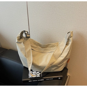 Detail of minimalist beige nylon crossbody bag with orange label on black leather sofa
