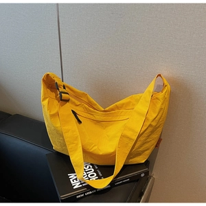 Detail of bright yellow nylon hobo bag with adjustable black strap on a leather sofa