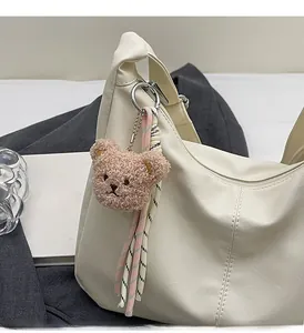 Close-up of a cute plush bear charm attached to a cream faux leather tote bag