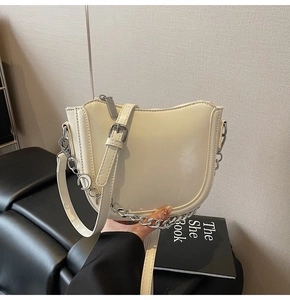 Detail of cream saddle bag featuring silver metal chain and adjustable leather strap