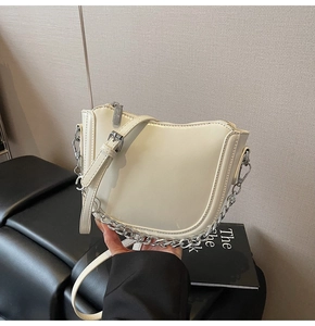 Detail of a creamy white crescent shoulder bag with silver chain and adjustable strap