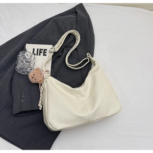 Detail of cream leather hobo bag with teddy charm and ribbon on gray blazer background