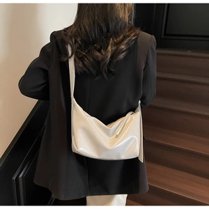 Model wearing a minimalist cream glossy crossbody bag over a black blazer back view