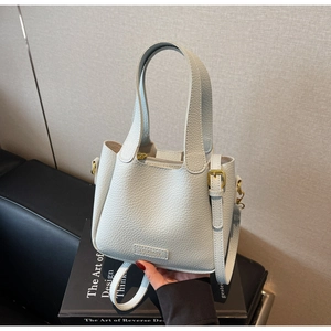 Detail of light gray lychee grain leather bucket bag with gold hardware and brand logo