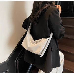 Detail of glossy beige patent leather hobo bag on shoulder with wide adjustable strap
