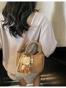 Borsa a mano kaki motivo litchi con chiusura dorata e ciondolo orsetto indossata da modella