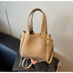 Detailed macro view of light brown litchi grain leather bucket bag with top handle and logo