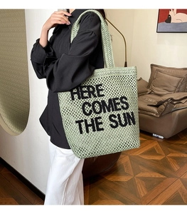 Detail of green woven tote bag with Here Comes The Sun embroidery and long straps