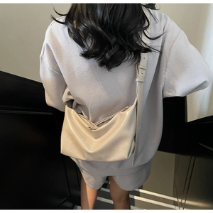 Model wearing a large cream off-white glossy hobo bag with adjustable crossbody strap