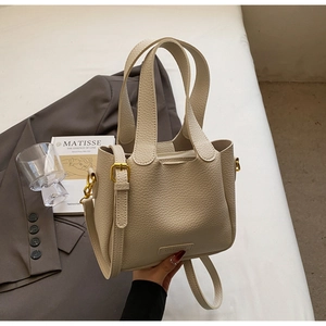 Detailed close-up of cream-colored lychee leather bucket bag with gold-tone hardware