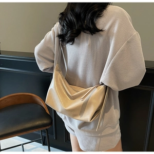 Model showing a large beige pleated shoulder bag with glossy finish in an indoor setting