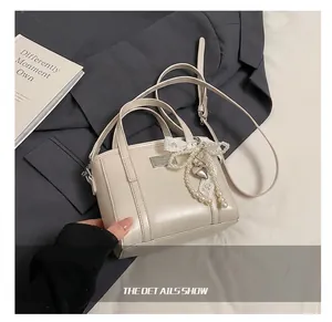 Detailansicht der cremefarbenen PU-Lederbeuteltasche mit Perlenbogen und Metallanhänger
