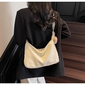 Close-up of cream white tote bag with textured faux leather and plush ball pendant