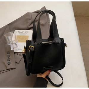 Detail of black lychee grain bucket bag with gold hardware and zipper on a grey background
