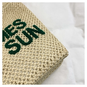 Detailed close-up of straw woven texture and green SUN embroidery on a beach bag