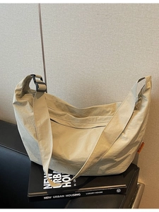 Minimalist beige nylon tote bag with wide shoulder strap on a sleek urban background
