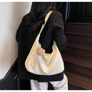 Detailed side view of cream white tote bag with bear charm and woven rope detail
