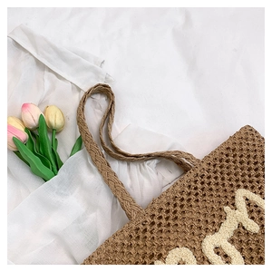 Dettaglio borsa tote in paglia con scritte ricamate crema e manici circolari