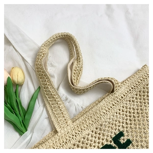Detail of woven straw tote bag featuring green embroidered letters and hollow texture