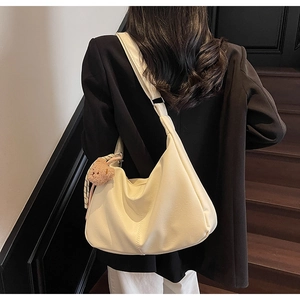 Close-up of a cream crescent shoulder bag with vertical stitching and a bear charm accessory