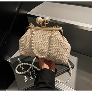 Detail of hand-woven beige straw clutch with golden metal frame and large pearl clasp