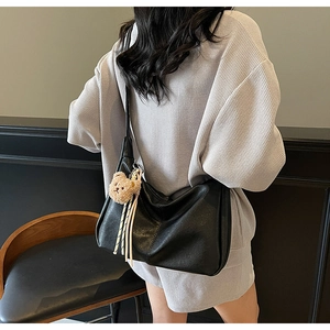 Lifestyle view of a black soft leather hobo bag with a plush bear and striped ribbon