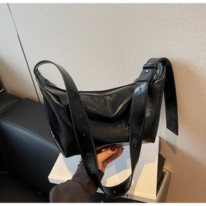 Detail of glossy wrinkled leather texture and wide adjustable strap on black shoulder bag