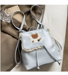 Close-up of light blue backpack with lace trim, teddy bear patch and drawstring closure
