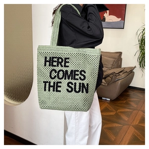 Close-up of 'HERE COMES THE SUN' embroidery on green woven straw beach tote bag