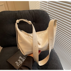 Close-up of cream hobo bag with adjustable wide strap on a textured black chair