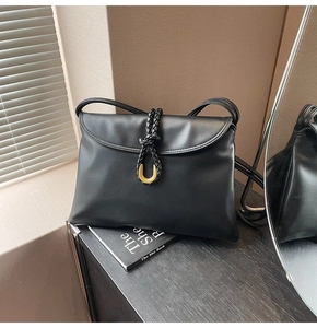 Detail of black leather shoulder bag featuring gold U-shaped buckle and woven knot trim