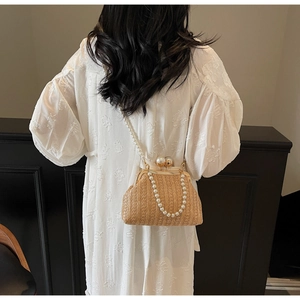 Detail view of woven straw bag with faux pearl strap on model wearing white dress