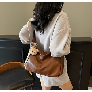 Close-up of brown leather tote bag with a plush bear charm and striped ribbon detail