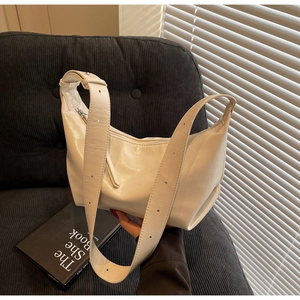 Detail of white crescent shoulder bag with wide grommet strap on a textured sofa