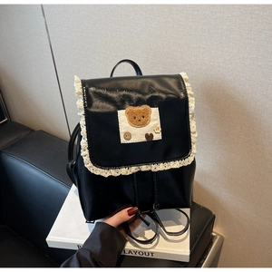 Detail of black PU leather backpack with white lace edges and a cute plush bear charm