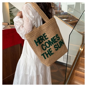 Detail of embroidered green 'HERE COMES THE SUN' lettering on large straw tote bag