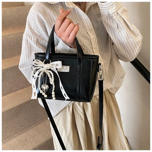 Detailansicht der schwarzen Lackledertasche mit Spitzenschleife und Perlenanhänger