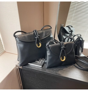 Detailed view of black matte leather shoulder bag with woven strap and gold metal buckle