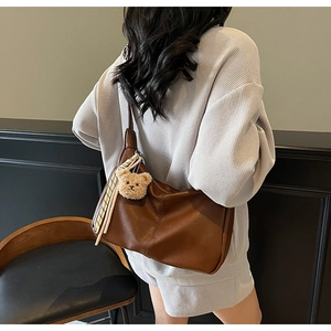 Detail of a large brown PU leather tote bag with plush bear charm and ribbon accent