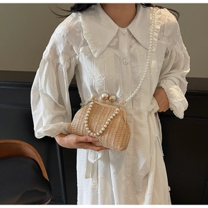 Detail of straw woven bag with metal clasp and large pearls on a white blouse
