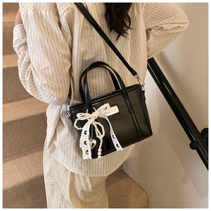 Detail der schwarzen Kunstledertasche mit weißer Spitzenschleife und Perlenanhängern