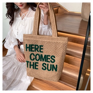 Close-up of straw tote bag with green embroidered HERE COMES THE SUN text on stairs