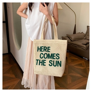 Detail of embroidered 'HERE COMES THE SUN' text on large woven straw beach tote bag