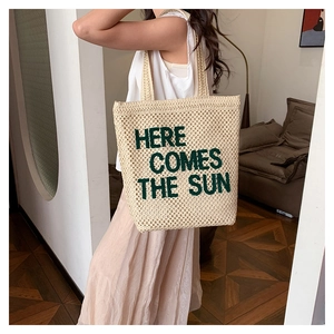 Detail of embroidered 'HERE COMES THE SUN' text on large beige woven beach tote bag