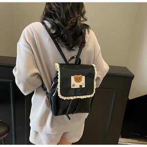 Detail eines schwarzen Kunstlederrucksacks mit weißem Spitzenbesatz und Bären-Aufnäher