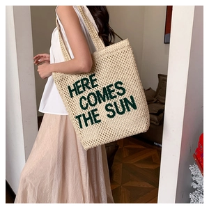 Detail of embroidered 'HERE COMES THE SUN' text on large woven straw beach tote bag