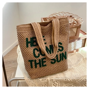 Detail of woven straw tote bag with green embroidered Here Comes The Sun lettering