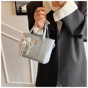 Details einer hellblauen glänzenden Handtasche mit Schleife und Perlenanhänger