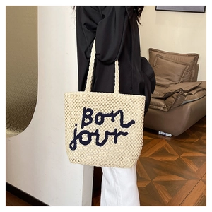 Dettaglio della borsa tote in paglia beige con ricamo bonjour e manici intrecciati