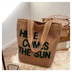 Detail of beige straw tote bag featuring green Here Comes The Sun embroidery